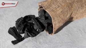 Black BioWoodTech charcoal pieces spilling from a burlap sack onto a textured gray surface, showcasing sustainable biomass fuel.