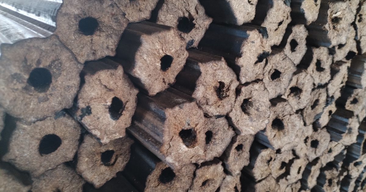 Stacked hexagonal sawdust wood briquettes with central holes.