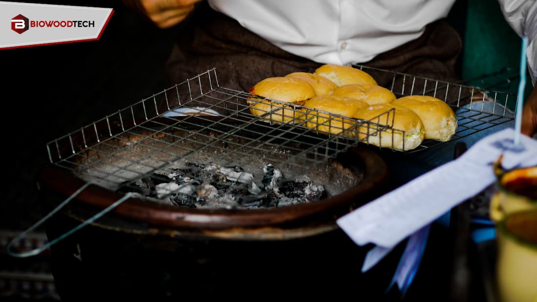 A professional charcoal grill with glowing embers and a wire rack holding buns, showcasing Biowoodtech’s premium restaurant-grade charcoal in a commercial food setting.